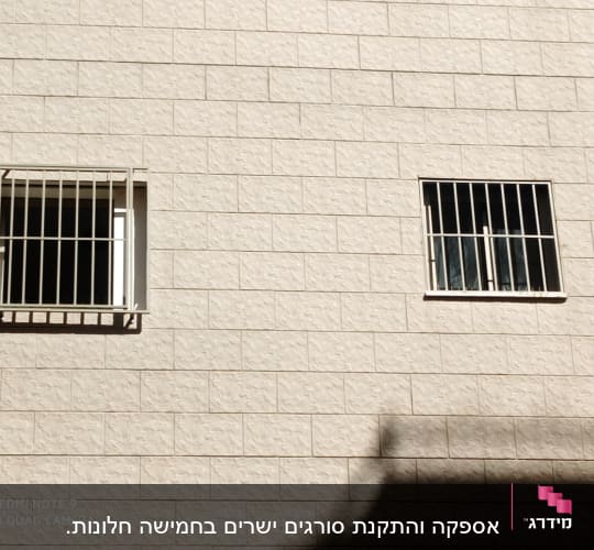 שני חלונות עם סורגים על קיר לבנים